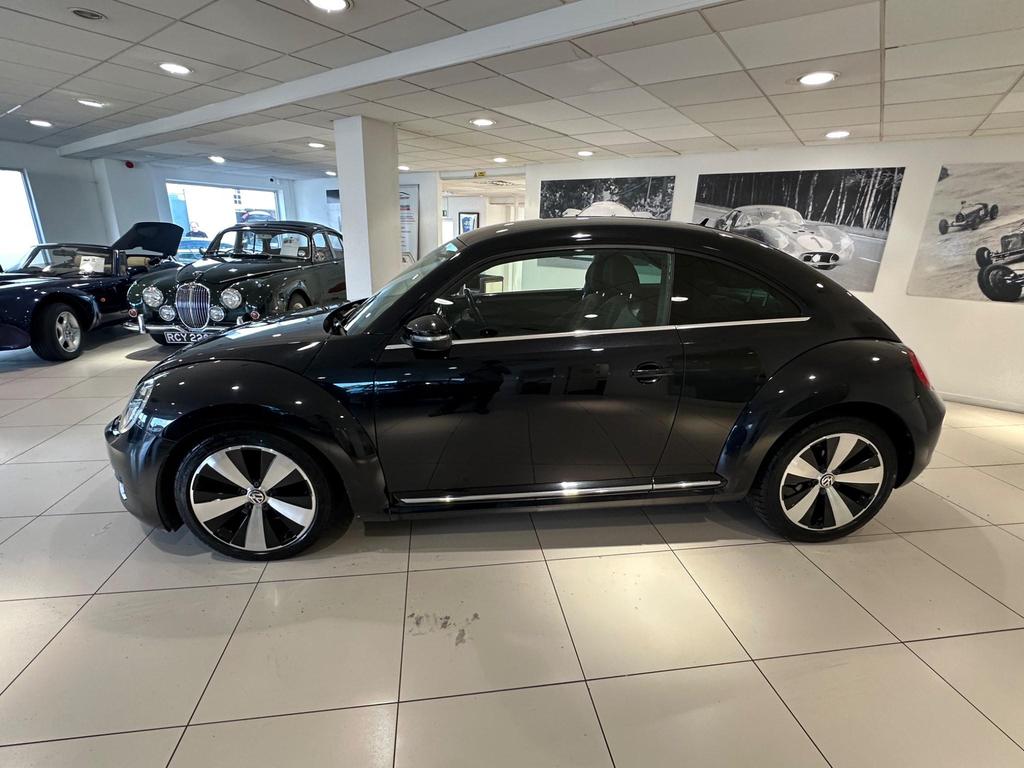Front view of the 2013 Volkswagen Beetle in sleek black, showcasing its iconic design and alloy wheels.