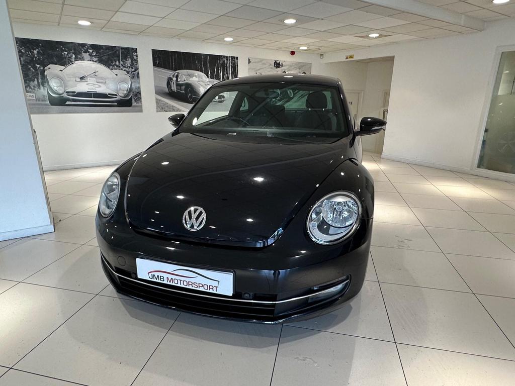 Front view of the 2013 Volkswagen Beetle in sleek black, showcasing its iconic design and alloy wheels.