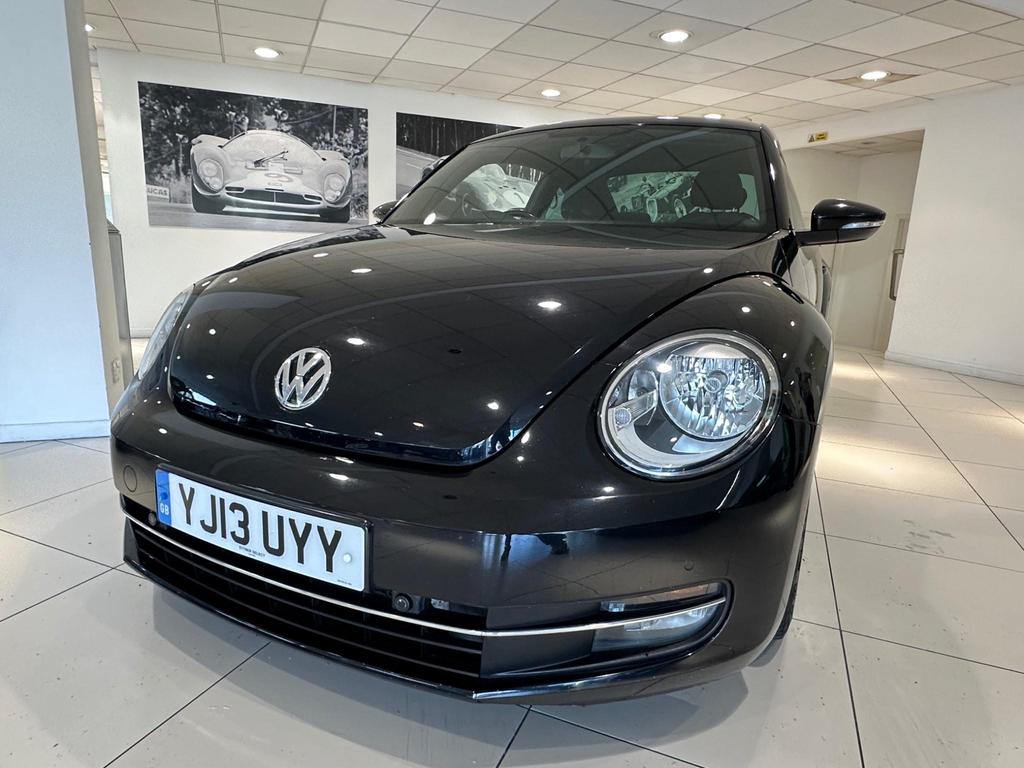 Front view of the 2013 Volkswagen Beetle in sleek black, showcasing its iconic design and alloy wheels.